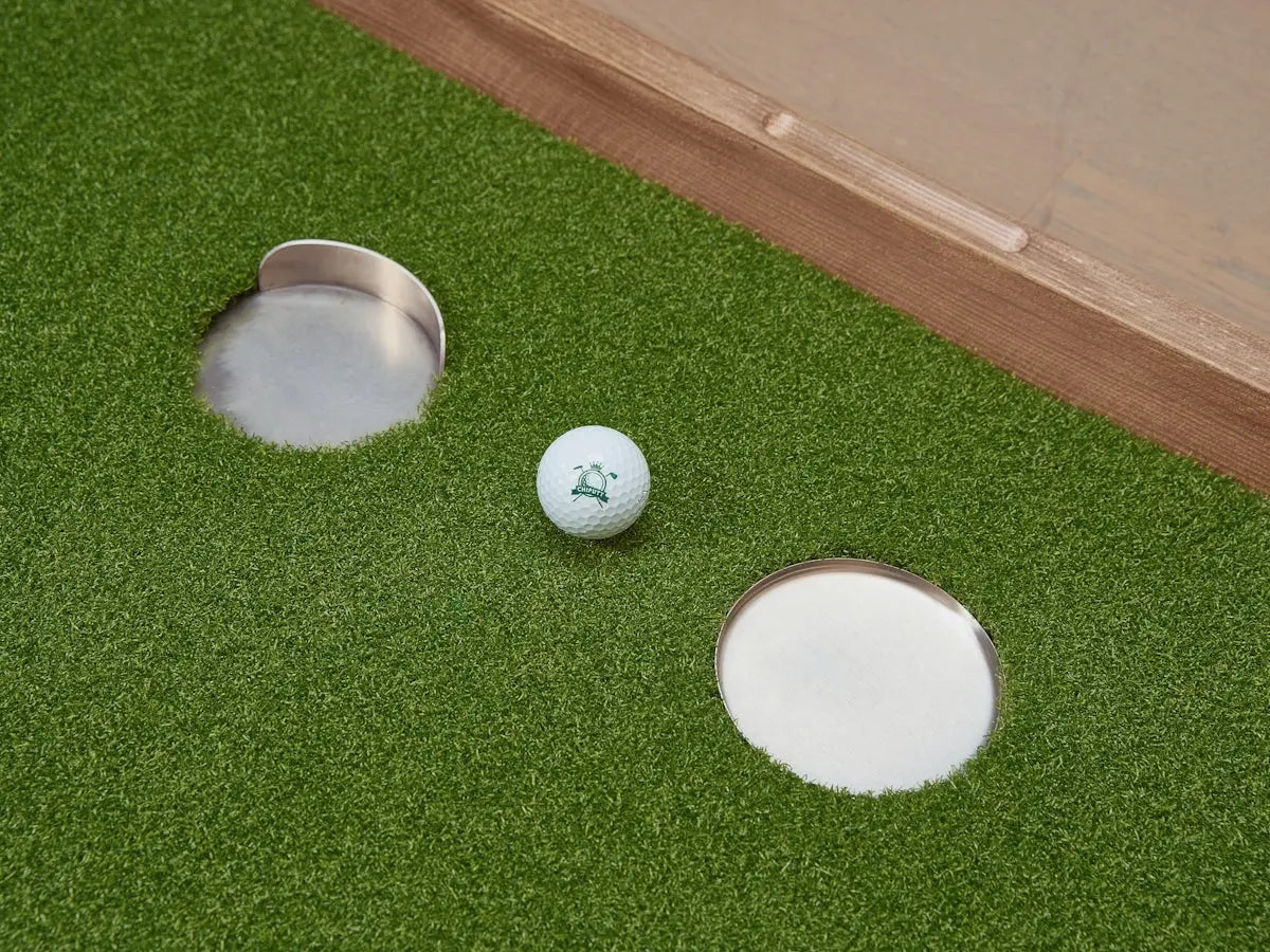 Golf ball near two holes on green turf