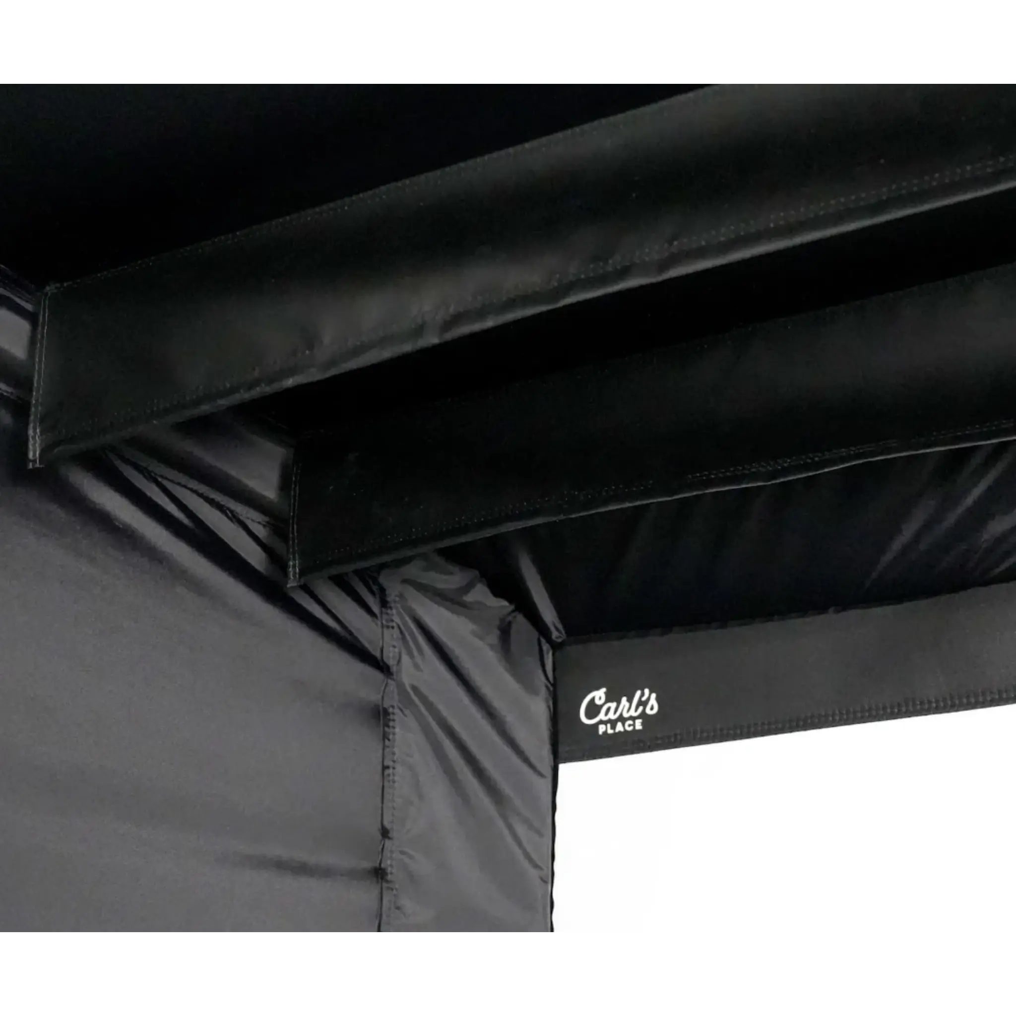 Close-up view of the top section of a black golf simulator enclosure with sturdy nylon fabric and connector fittings. The enclosure features a logo that reads Carls Place, emphasizing its professional quality and design.