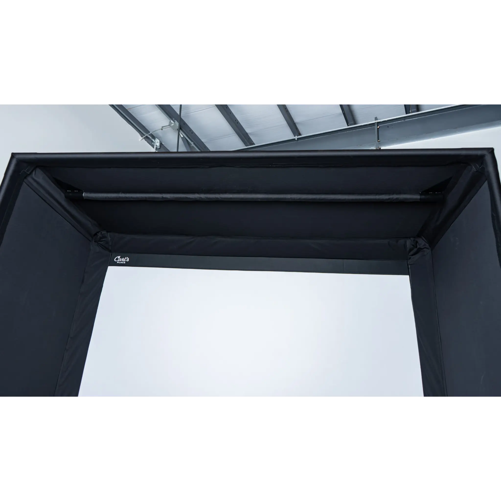 A close-up view of the top section of a black golf simulator enclosure, featuring a sturdy frame and a smooth, white backdrop. The setup is designed for indoor golfing, emphasizing professional durability and immersive play.