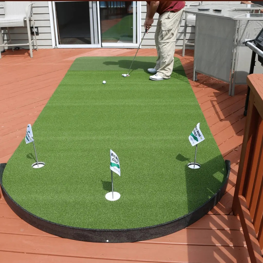 Person putting golf ball at home on a Big Moss Commander Patio Series 615 green with three flagged holes visible