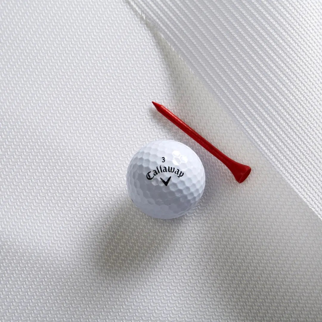 A white Callaway golf ball and a red tee rest on a textured golf impact screen surface