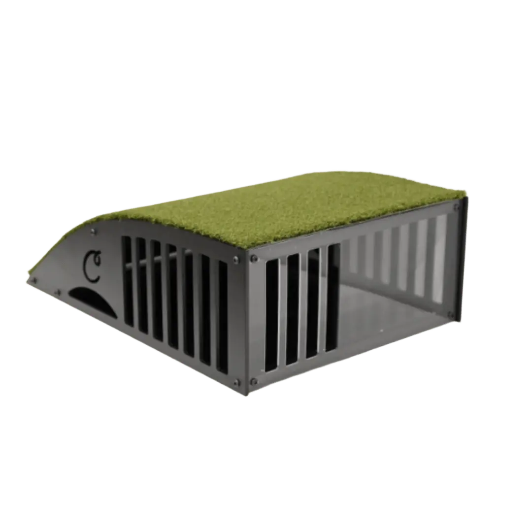 Black plastic trap with a grated opening and surrounding green turf, similar to a floor mounted projector enclosure.