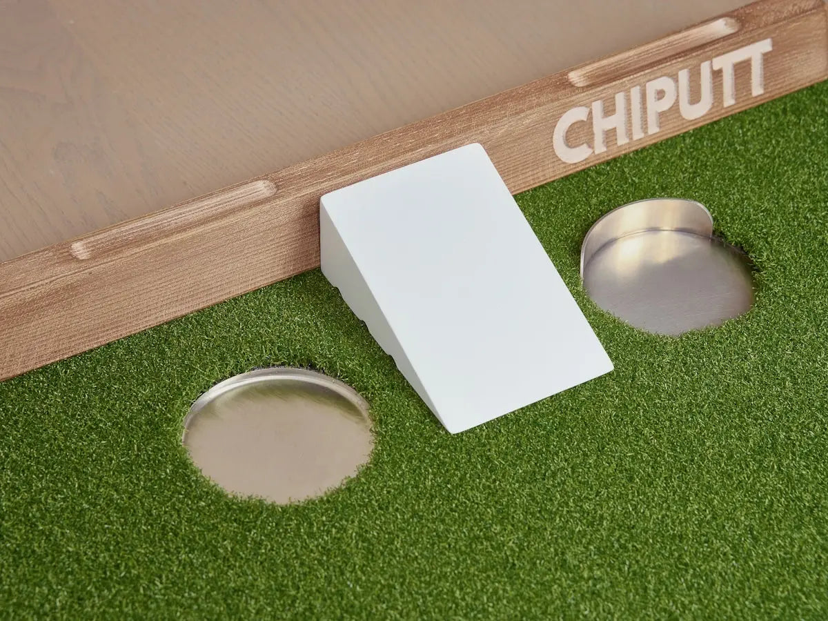 Putting green with two holes and a white wedge.