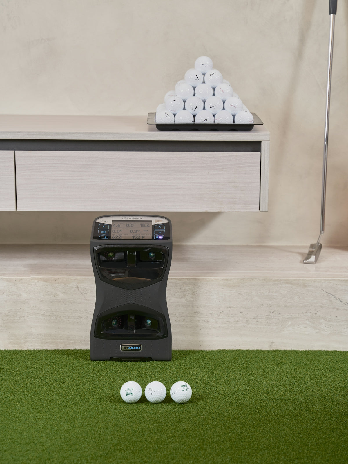 Golf ball dispenser with golf balls on green turf.