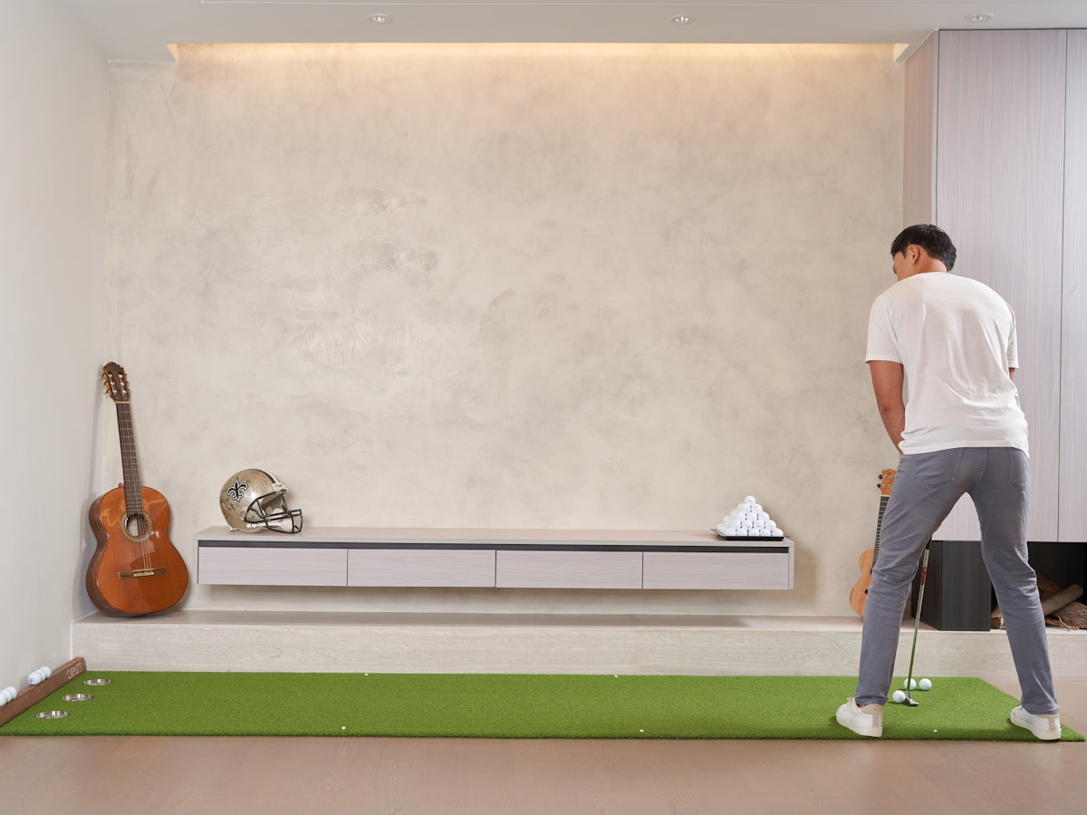 Man practicing golf putt indoors on green mat.