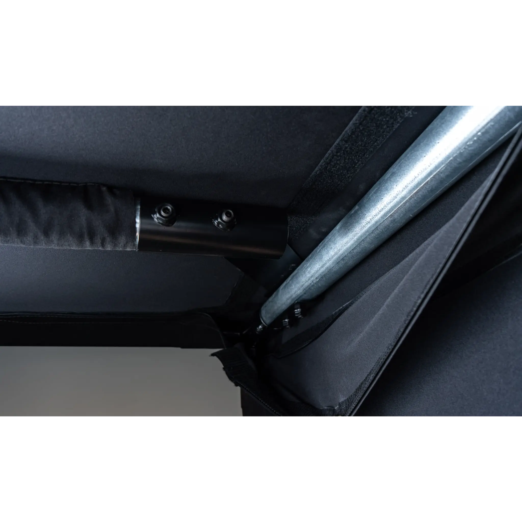 Close-up view of a black fabric and metal frame structure, highlighting the connection points where the fabric meets a sturdy metallic rod. The material appears durable, suitable for a professional-grade golf simulator setup.